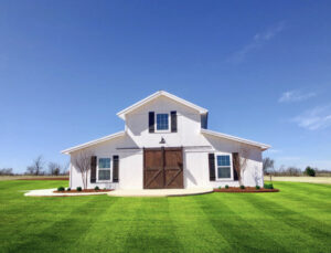 White and brown polebarn building with a large front porch and well-maintained lawn