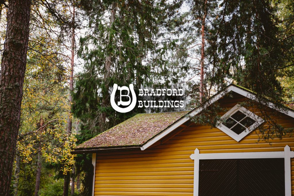 A yellow wooden building with a mossy roof stands among tall trees. Overlaid white text reads "Bradford Buildings" with a circular "B" logo.